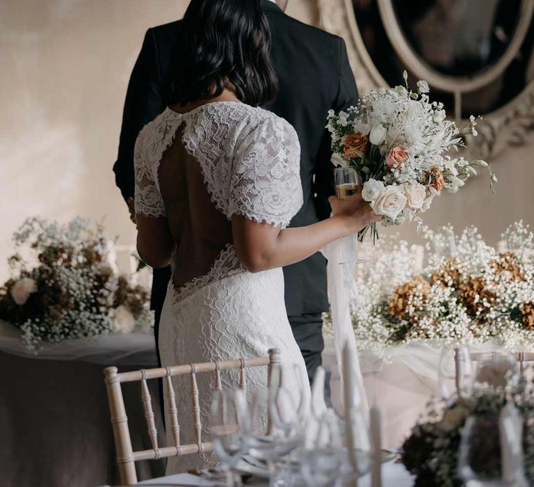 Bride in elegant open back lace wedding dress holding rose, eucalyptus and baby's-breath floral bouquet 