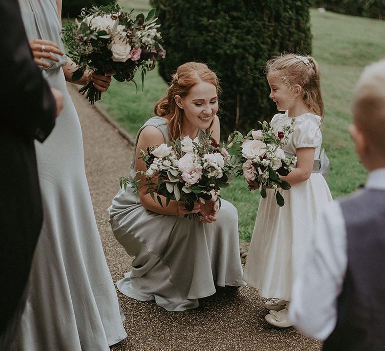 Bridesmaid in sage green bridesmaid dress kneels down to flower girl 