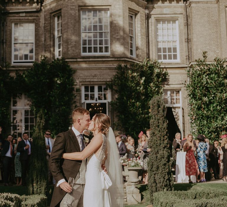 Bride in Savannah Miller wedding dress and groom kiss as guests gather in the grounds of Hedsor House