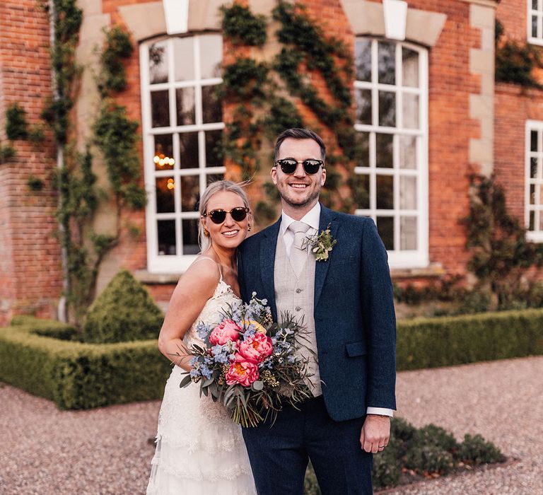 The bride in a lace wedding dress with the groom in a navy and grey suit wearing cool wedding sunglasses for botanical greenery theme wedding 