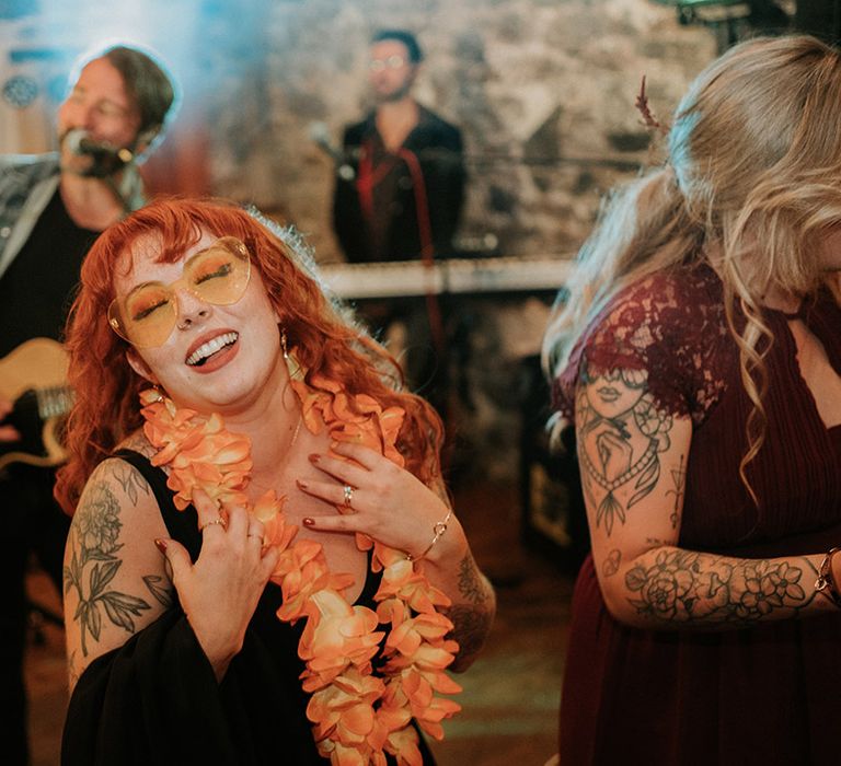 Bride in v-neck black wedding dress, orange wedding lei and orange wedding sunglasses dancing 