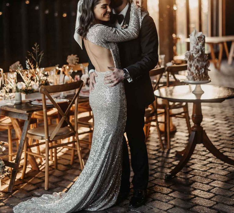 Groom in classic black tuxedo dancing with bride in open back silver sparkly wedding dress and large hair bow accessory 