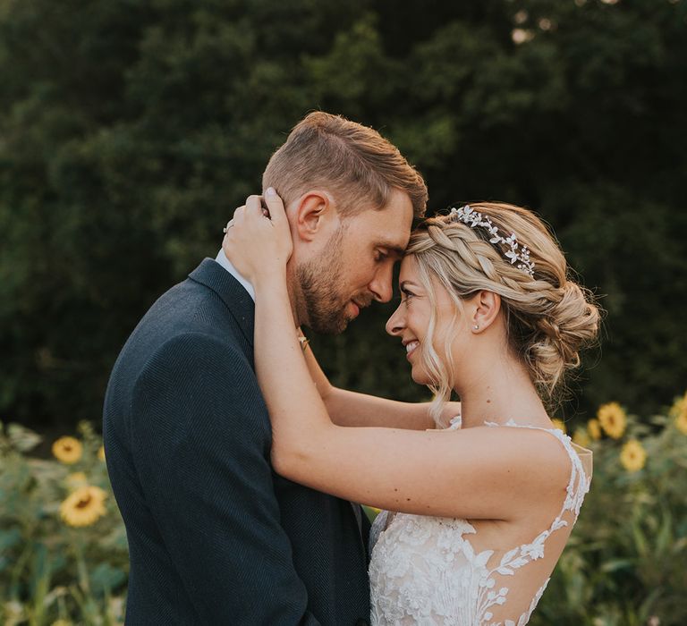 The bride with her blonde hair in a braided updo with sparkly headpiece in a illusion lace wedding dress and the groom in a dark blue suit 