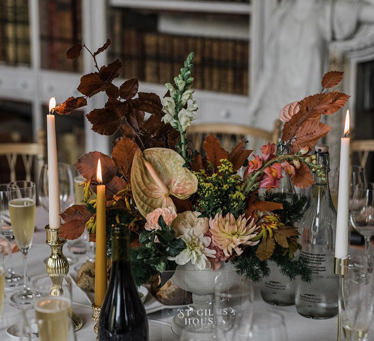 Anthuriums, dahlias, and autumnal leaves make up the wedding table centrepiece with taper candles for cosy vibes 