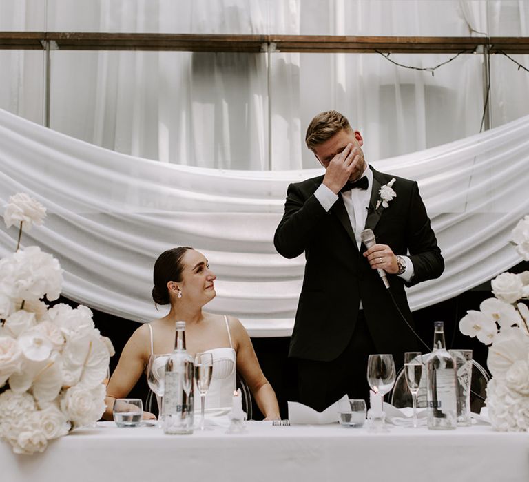 The groom in traditional black tie stands and gets emotional as he reads out his wedding speech 