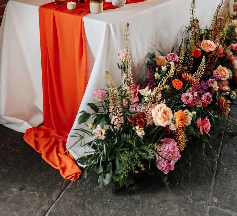 Retro wedding tablescape with pink tapered candles, orange table runner, mismatched single flower vases, colourful flower centrepieces and large colourful flower arrangements Northern Monk Refectory Leeds