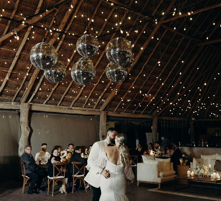 bride in a mermaid wedding dress kissing her groom in a white dinner jacket enjoying their first dance in a wooden Mexican palapa hut with firelight ceiling decoration 