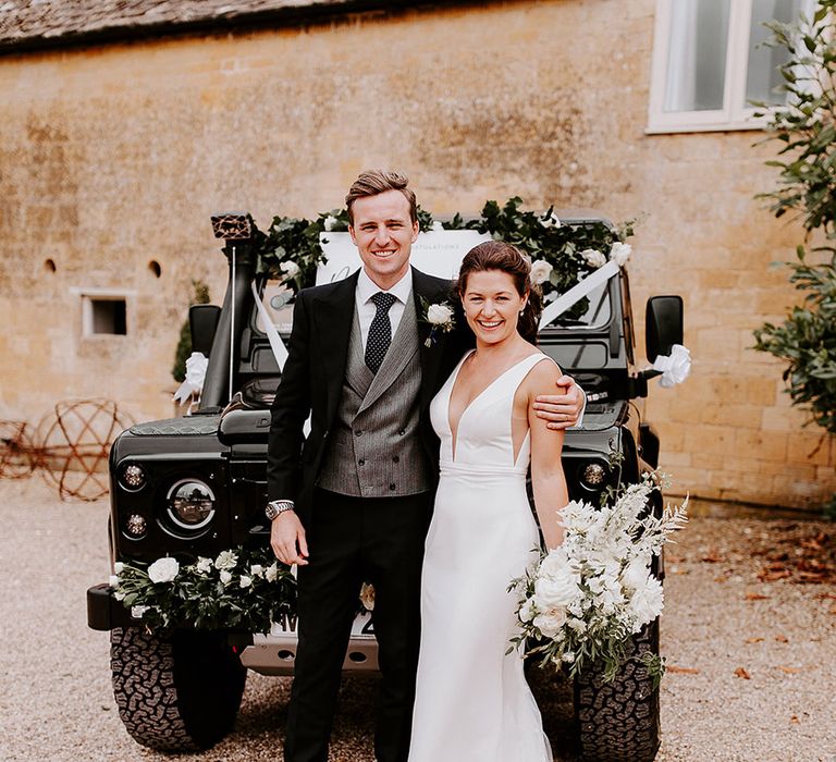 Landrover Defender black wedding car with the bride and groom posing in front of the car at Lapstone Barn 