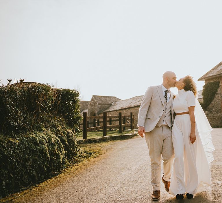 Groom in cream three piece wedding suit with spotted tie kissing bride in two piece separates 