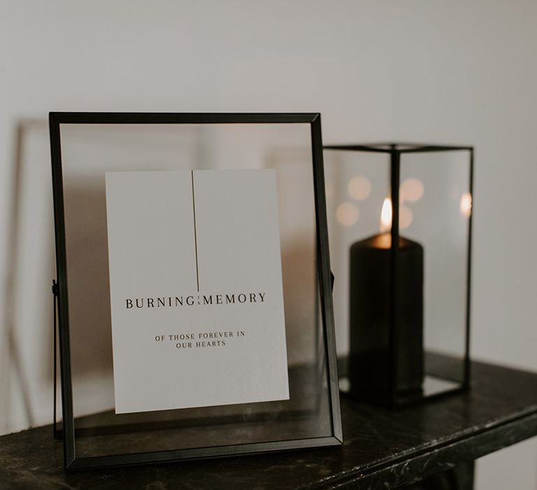 Black pillar candle in black square lantern next to sign to memorialise lost loved ones