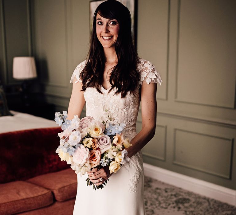 Pastel pink, blue, yellow, and white wedding bouquet held by bride in lace wedding dress 