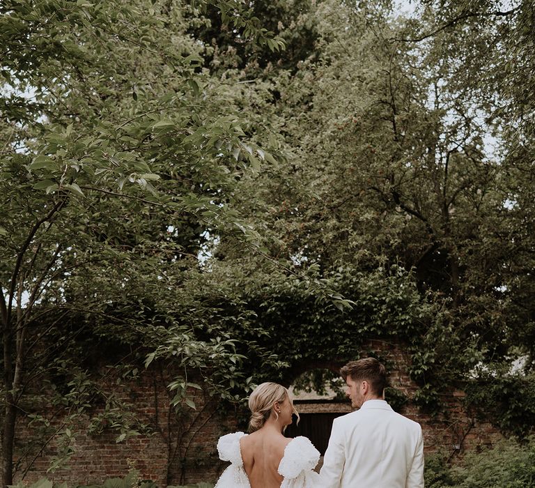 The bride walks in a Chosen by Kyha wedding dress with detachable puff sleeves with groom in white tuxedo