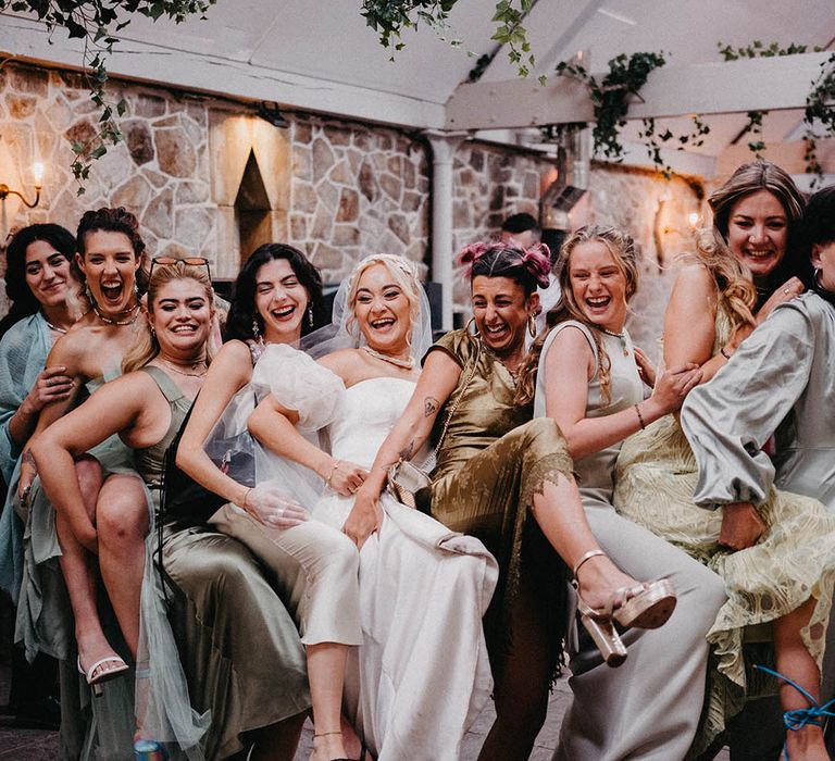 The bridal party pose together in green satin and tulle mismatched dresses at the wedding reception 