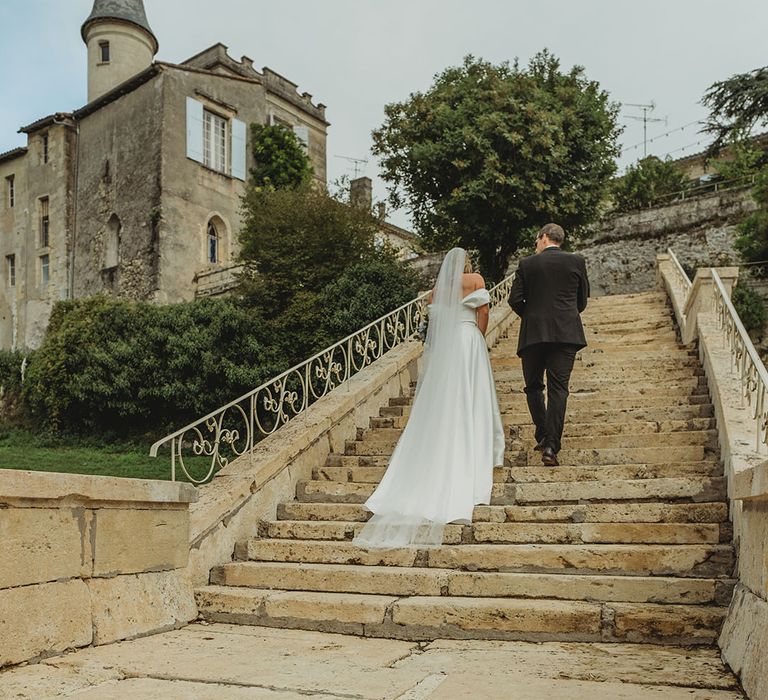 The newlyweds walking up the stairs of their chateau wedding venue 