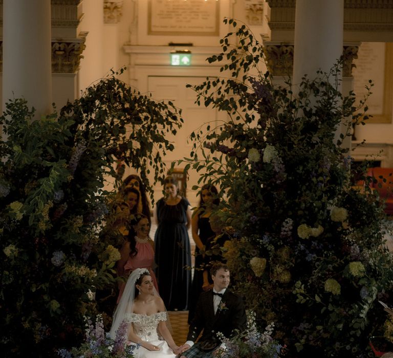 Botanical floral wedding decorations with foliage and purple flowers lining the aisle and altar 