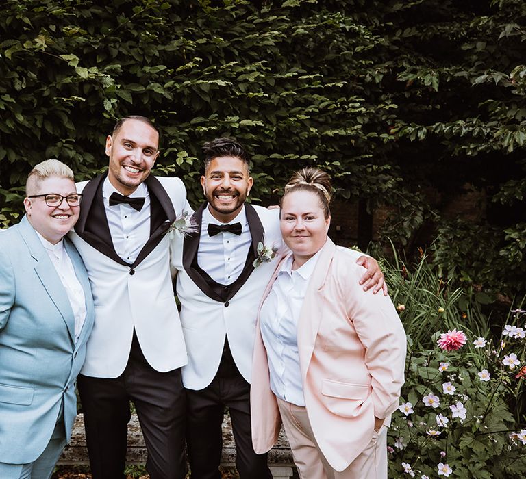 The two grooms pose with their wedding guests in pink and blue suits 