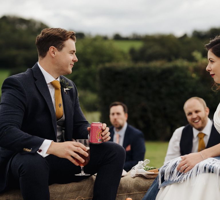 Bride & groom sat on hay bales in garden with wedding guests 