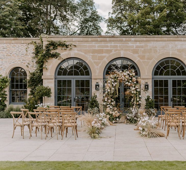 Outdoor wedding ceremony at Dewsall court with wooden chairs and floral aisle and altar decor 