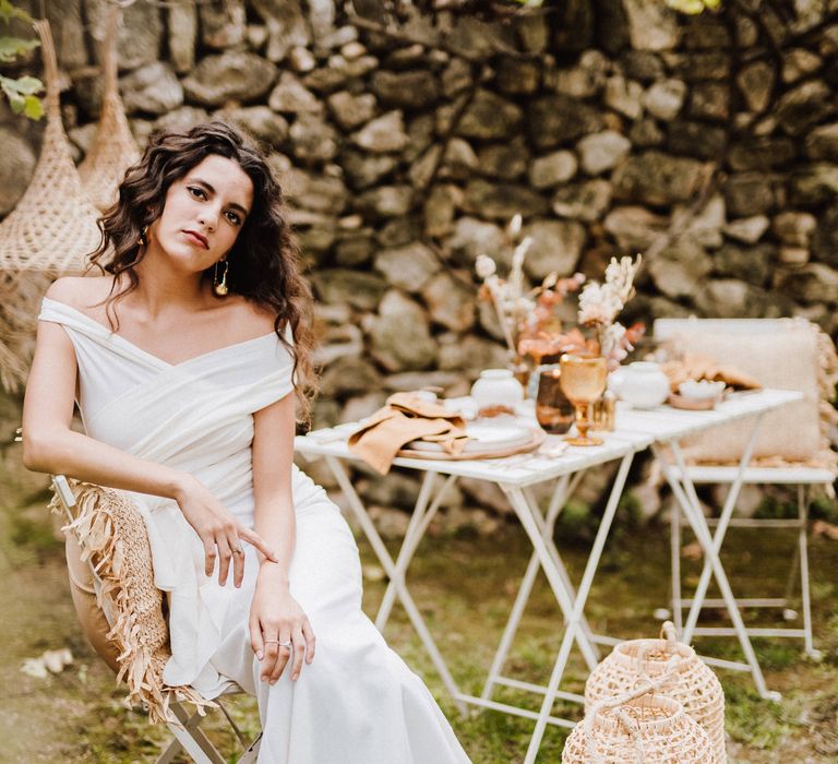 Bride sits outdoors in Mallorca next to woven candle holders