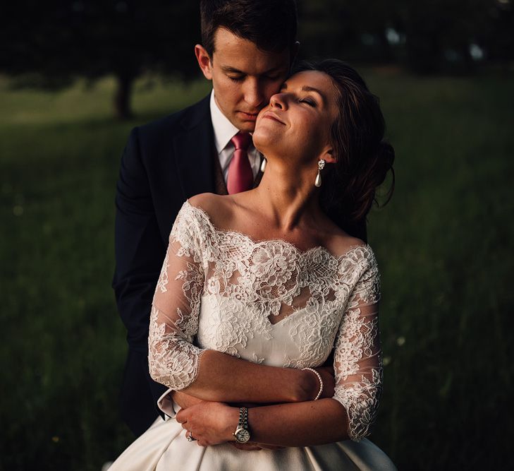 Brown haired bride wears lace wedding gown while groom wraps his arms around her