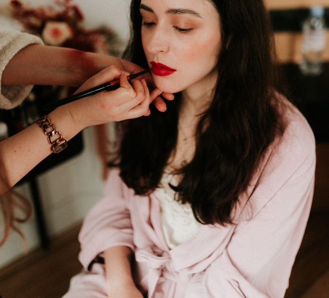 White bride with long brown hair having her red lipstick and brown eyeshadow makeup done. | Anne-Sophie Benoit Photography