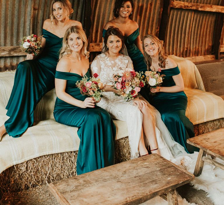 Relaxed portrait of the bride and her bridesmaids sitting on hay bales at an autumn themed wedding in Devon 