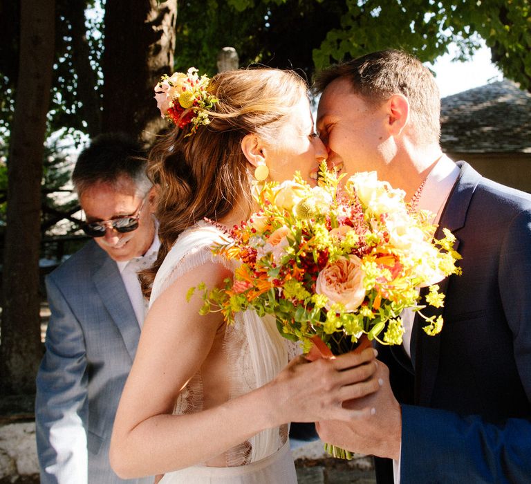 The bride and groom share a kiss behind her bouquet