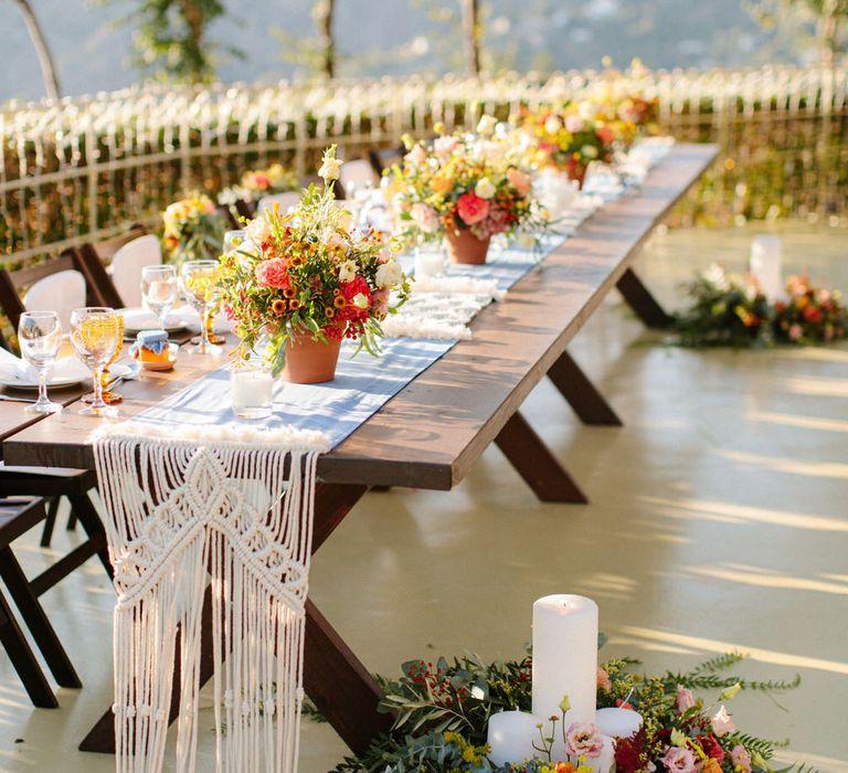 Wooden monastery banquet table with macrame decor and linen table runner at this destination wedding in Greece