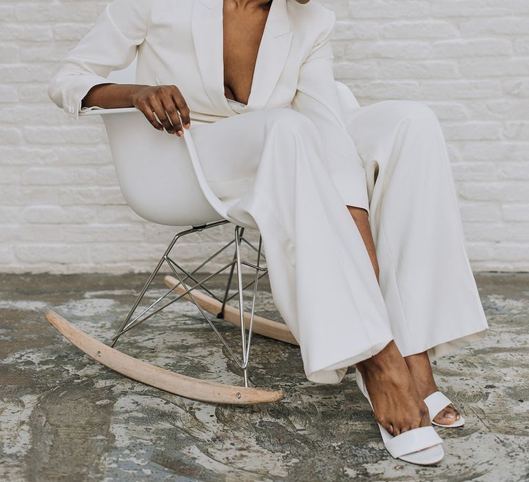 Bride wearing a sleek white bridal suit sitting in a modern rocking chair