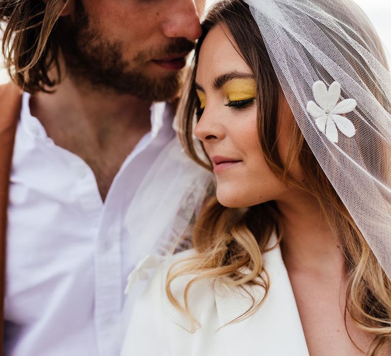 Groom with long hair kissing his bride with yellow wedding eyeshadow wearing an appliqué veil