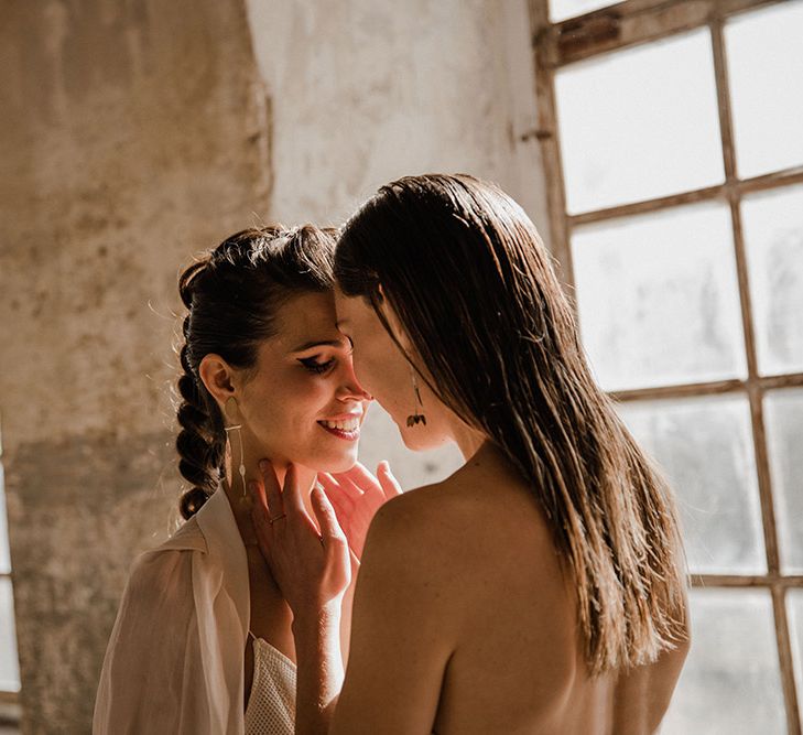 Intimate wedding photograph of two brides with sleek straight hair and braided updo