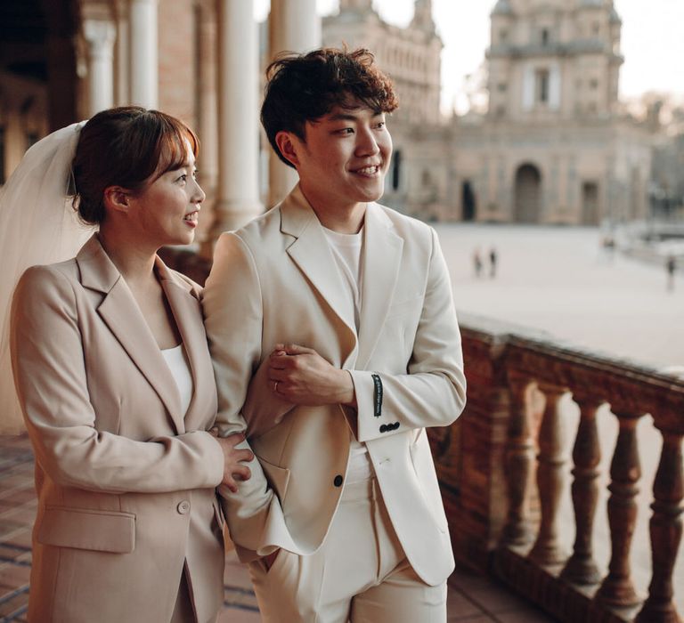 Asian woman wearing veil and pink suit and partner wearing cream suit