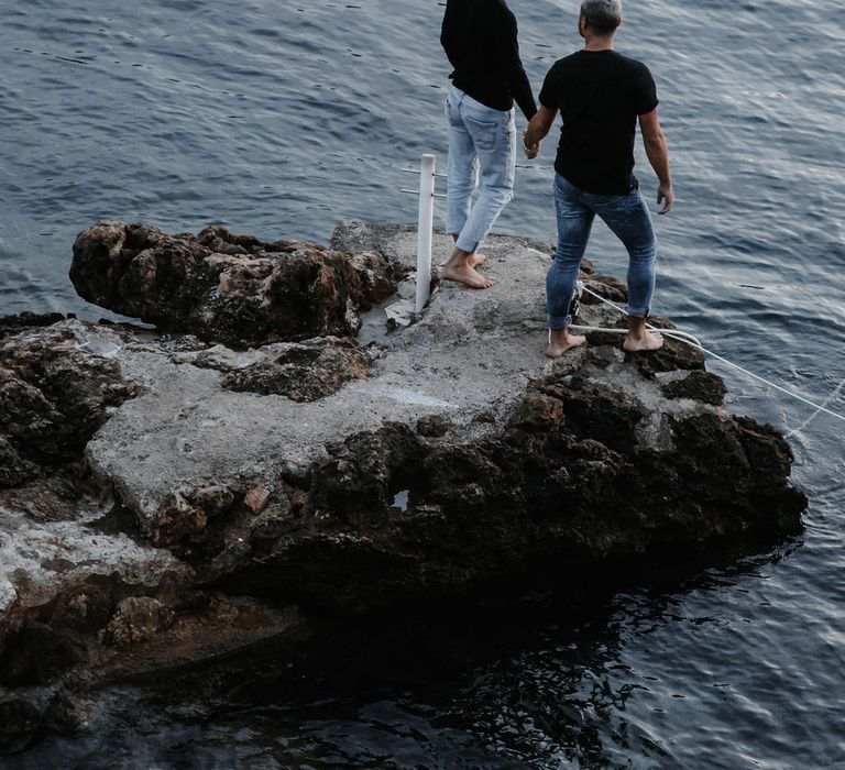 Grooms stand upon the rocks and look out to sea in Ibiza