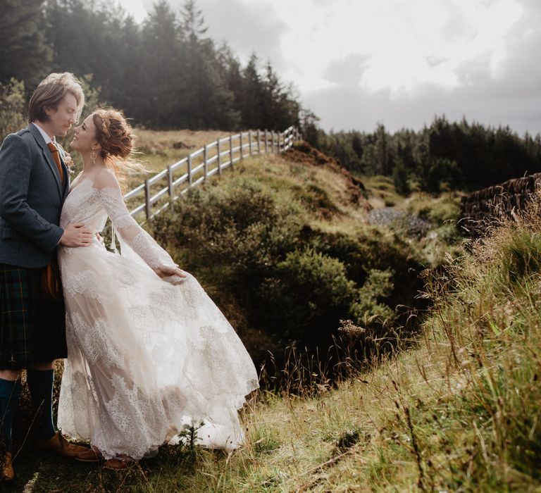 Bride & groom stand on the hillside as the sun shines