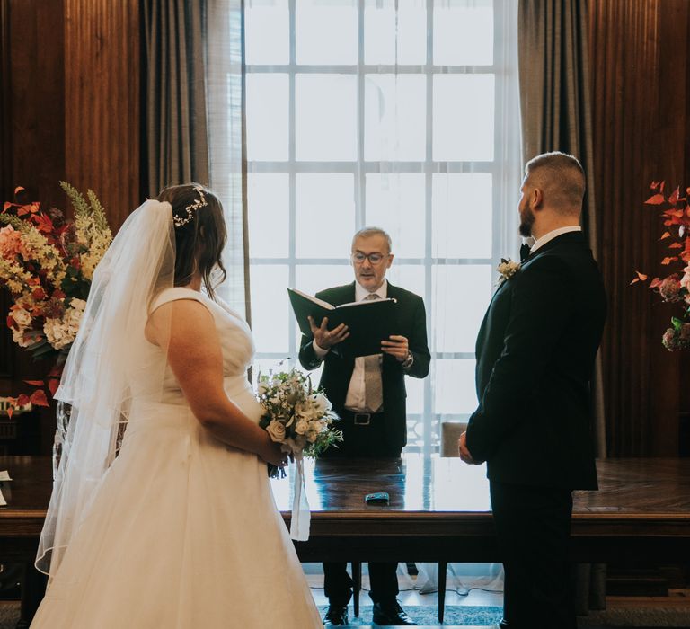 Bride & groom stand in front of altar as celebrant reads during wedding ceremony