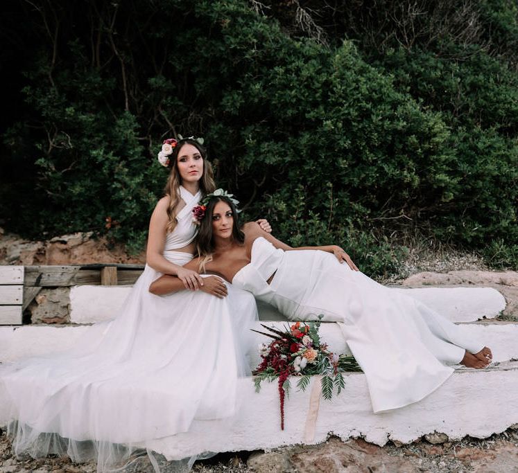 Two brides on the beach in Ibiza, one is laying across the other's lap