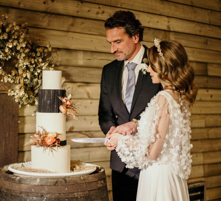 Bride and groom cutting into black and white four tier wedding cake by Amalina Bakes