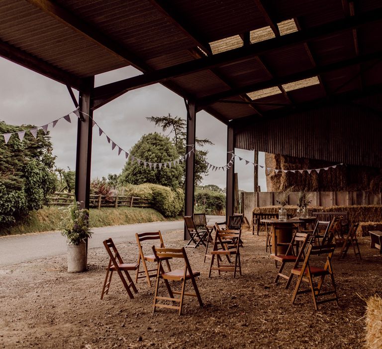 Interior of barn decorated for home farm wedding with bunting, hay bales and wooden chairs and tables