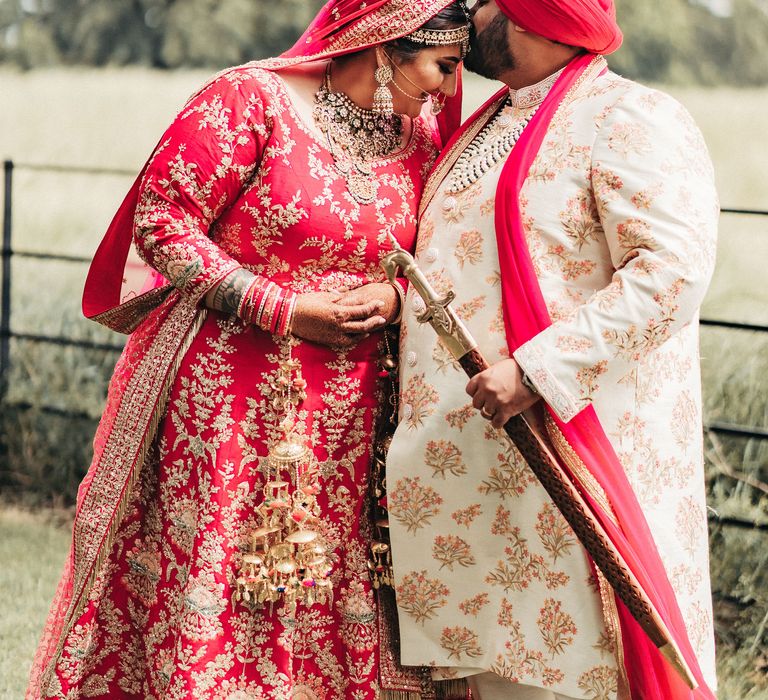 Groom kisses bride on the forehead as they stand outdoors with one another for portrait photos