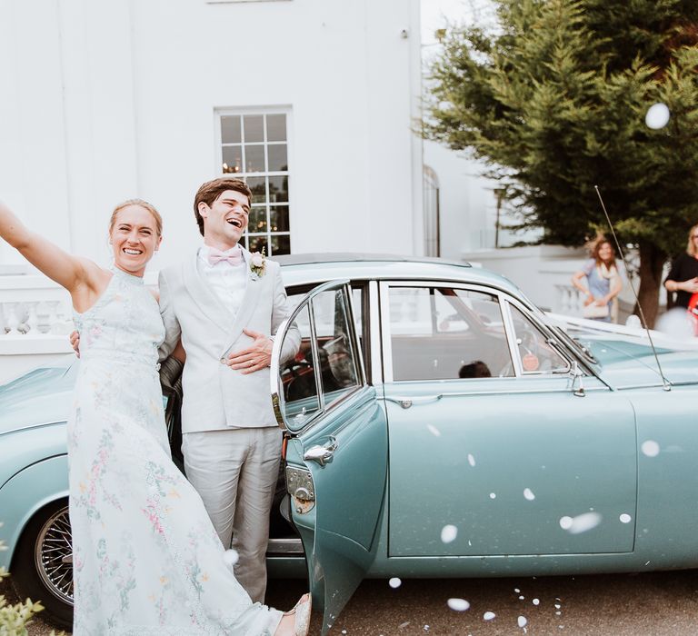 Bride & groom stand beside vintage car on the day of their wedding