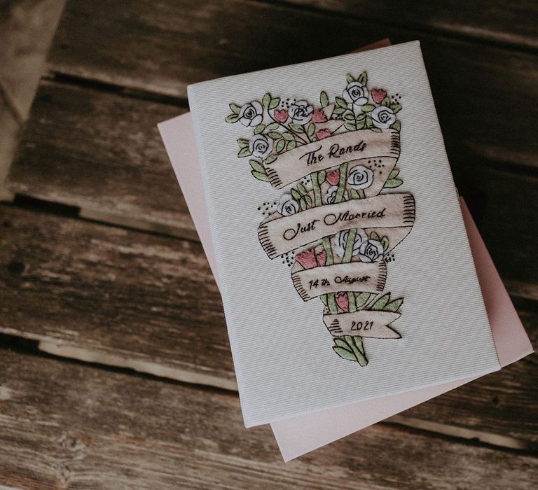 White card embroidered with white and pink floral bouquet and ivory ribbon reading 'The Rands Just Married 14th August 2021' for Surrey summer wedding