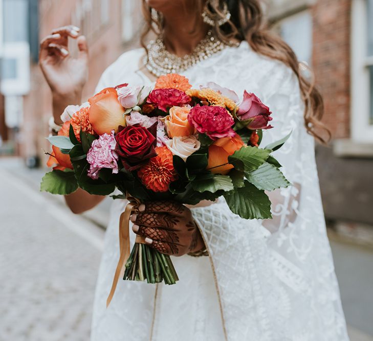 A brightly coloured bouquet made up of pink orange and red flowers for Indian British wedding.