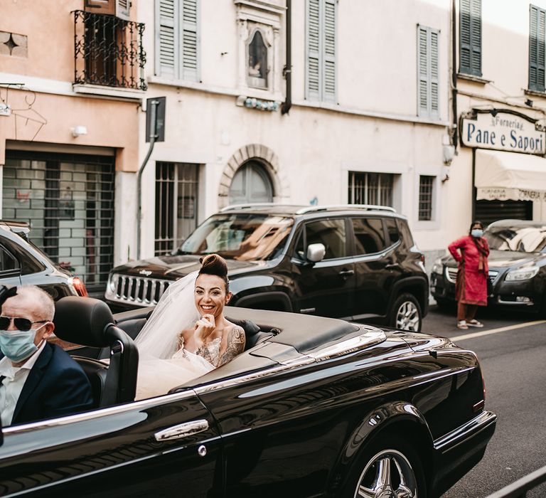 Bride smiles as she rides in sleek black car on her wedding day