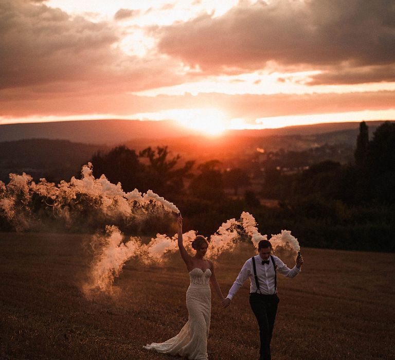 Dewsall Court wedding with bride and groom holding white smoke bombs in the air during golden hour 