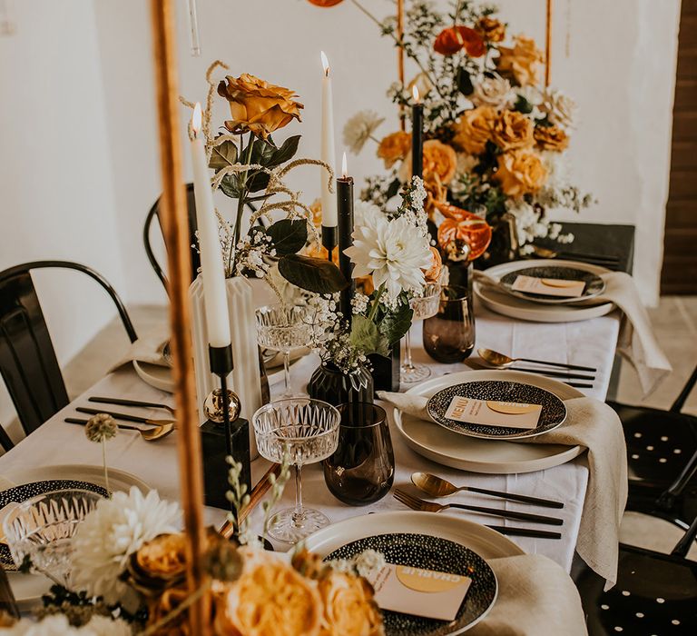 Wedding table decor with black candlesticks and taper candles, crystal coupe glasses and gold cutlery 