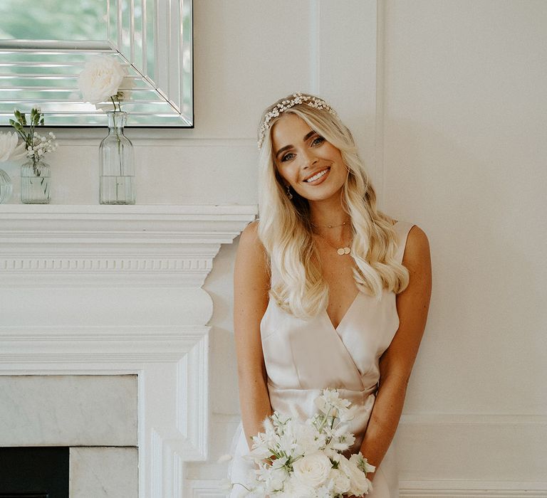 Bridesmaids with long blonde wavy hair wearing a hair vine and wrap satin bridesmaid dress holding an all white bouquet 