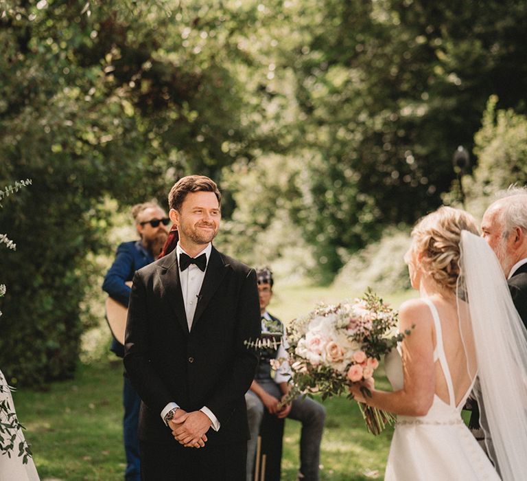 Groom in a tuxedo waiting at the altar for his bride in a Stella York wedding dress and cathedral length veil 