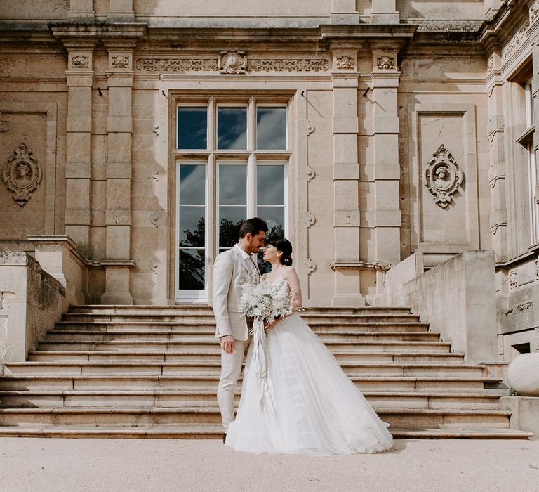 Classic wedding inspiration at Bylaugh Hall with groom in a stone check suit and bride in a tulle wedding dress holding a white wedding bouquet 