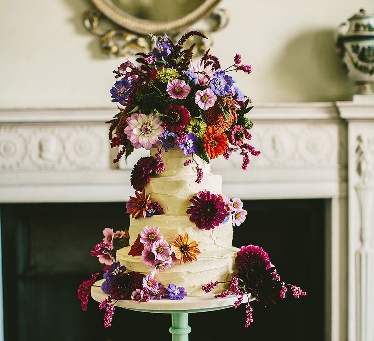 Four tier buttercream wedding cake on a green cake stand with an overflowed flower cake topper 