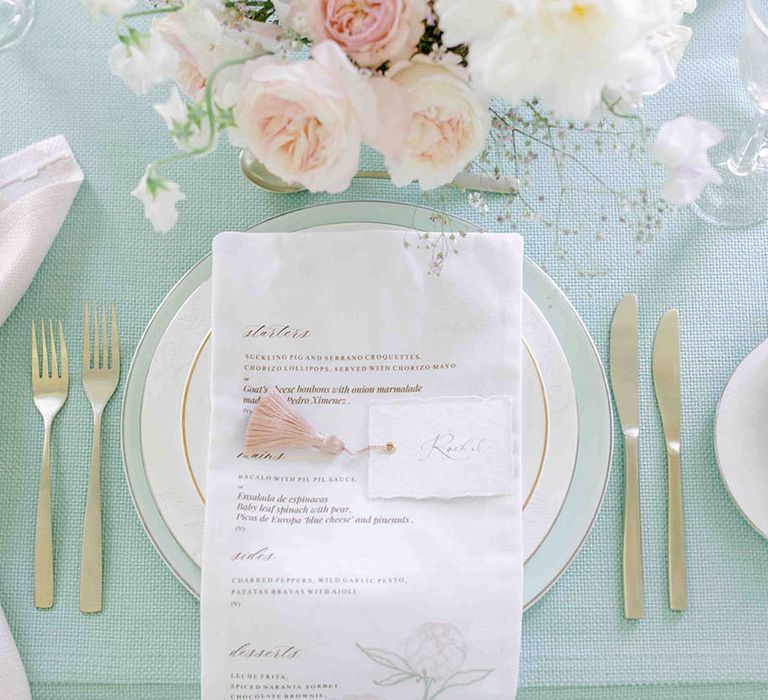 elegant place setting with gold rimmed plates, pale green tablecloth and fabric menu 